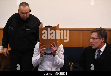 26 März 2018, Deutschland, Stade: Die Angeklagten des versuchten Mordes Mohamad Z. (L) zu seinem Sitz durch einen Gerichtsvollzieher in den Gerichtssaal, während Sie gleichzeitig ein Ordner vor seinem Gesicht geholt wird. Neben ihm ist sein Rechtsanwalt Reinhard Platzbecker (R). Z hat der absichtlich Auto fahren in einer Gruppe von Personen, die vor einer Diskothek im November 2017 ständigen beschuldigt worden. Sieben Menschen wurden verletzt. Foto: Carmen Jaspersen/dpa Stockfoto