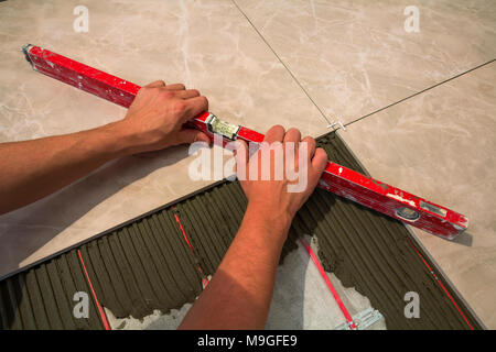 Keramische Fliesen und Werkzeuge für Fliesenleger. Arbeitnehmer hand installieren Bodenfliesen. Home Verbesserung, Renovierung - keramische Fliesen Kleber, Mörtel, Ebene. Stockfoto