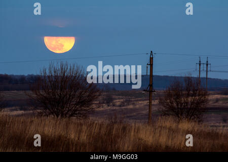 Große silberne leuchtende Mond close-up auf dunklen blauen Himmel mit vereinzelten Wolken. Neue Vollmond in der Nacht über Horizont mit Büschen und Leistungskabel lin Stockfoto