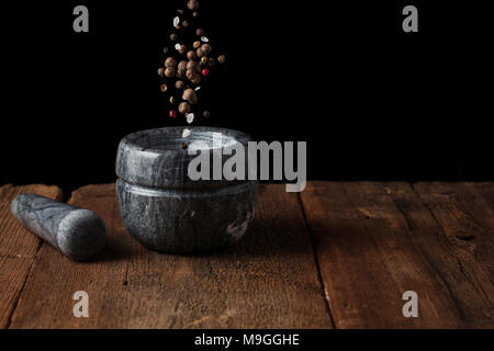 Marmor mörser auf alten Holztisch auf schwarzen Hintergrund mit kopieren. Pepper Samen fallen in den Mörtel. Gefrierschrank essen. Stockfoto