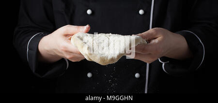 Köchin holding Hefeteig in ihren Händen auf schwarzem Hintergrund. Stockfoto