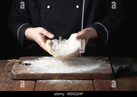 Köchin holding Hefeteig in ihren Händen auf schwarzem Hintergrund. Stockfoto