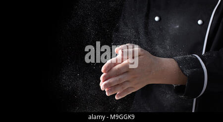 Koch Hände in Mehl auf schwarzem Hintergrund Banner. Die Pizza, Pasta, Brot backen und Süßigkeiten. Clap mit weißer Spritzer Mehl mit kopieren. Stockfoto