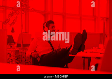 glückliche junge arabische Geschäftsmann mit Bart Musik hören über Kopfhörer in modernen Startup-Büro Stockfoto