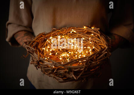 Frau tattoo Hände halten ein Nest Dekoration mit Licht auf dunklem Hintergrund Stockfoto