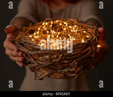 Frau Hände halten ein Nest mit Licht auf dunklem Hintergrund Stockfoto