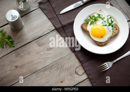 Spiegelei auf Vollkorn Toast und Kaffee zum Frühstück. Spiegelei mit Brot auf dem Teller über Holz- Tabelle, Ansicht von oben, kopieren. Stockfoto