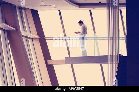 Junge erfolgreiche Geschäftsmann im Penthouse arbeiten an tbalet, moderne, helle Maisonette Büro Wohnung Interieur mit Treppe und große Fenster Stockfoto