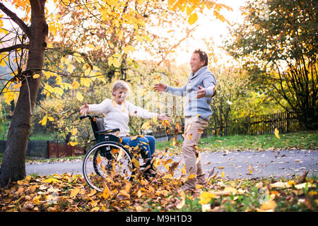 Senior Paar im Herbst Natur. Mann und Frau im Rollstuhl auf einem Spaziergang. Stockfoto