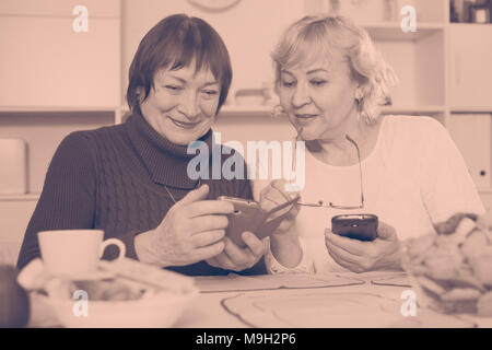 Zwei positive älterer Frauen mit Telefonen zusammen über Tasse Tee Stockfoto