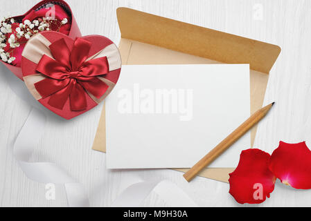 Mockup Kraftpapier Umschlag und einen Brief mit einer herzförmigen Geschenk mit roter Schleife und Rosenblättern, Grußkarte für Valentines Tag mit Platz für Ihren Text. Flach, Ansicht von oben Foto Mock up Stockfoto