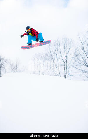 Bild von sportlichen Mann im Helm mit Snowboard in verschneiten Resort springen Stockfoto