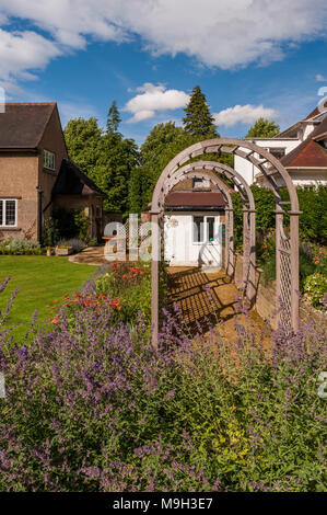 Sommer Blick auf die sonnenbeschienenen Tunnel Laube & bunte Staudenbeet - Schöne, gestaltet, gepflegten, traditionellen Garten, West Yorkshire, England, UK. Stockfoto