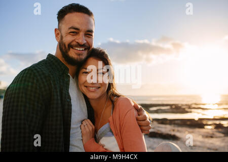Mann seinen Partner Holding mit seinen Arm um sie in der Nähe von einem Strand bei Sonnenuntergang. Mann und Frau genießen Sie Ferien in der Nähe der Küste. Stockfoto