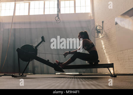 Passen junge Frau, die Arbeiten an einem rudergerät an der Turnhalle. Weibliche tun cardio übung im Fitness Club. Stockfoto