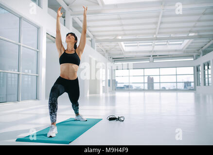 Gesundheitsbewusste frau yoga Ausfallschritt mit nach oben strecken darstellen, Virabhadrasana im Fitness Studio. Kaukasische Frauen trainieren Yoga in der Turnhalle. Warr Stockfoto