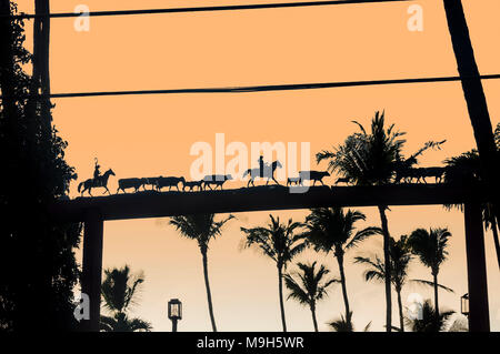 Cowboys auf dem Pferd März Rinder home bei Sonnenuntergang. Metall Kunst in Form von einem Fries auf ein Tor, Maui, Hawaii, USA Stockfoto