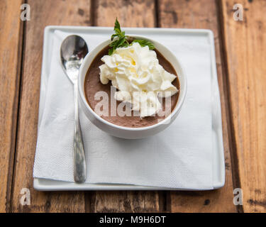Eine Schüssel mit braunen Schokoladenmousse, garniert mit Sahne sitzen auf braunem Holz Tisch. Stockfoto