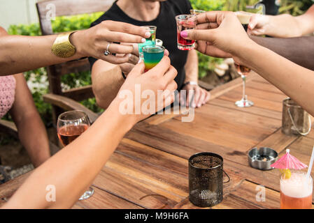 Eine Gruppe von Armen und Händen halten bunte Shot Gläser Alkohol kommen zusammen, während ein Toast. Eine Vielzahl von hauttönen gesehen werden kann. Stockfoto