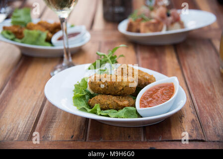 Nahaufnahme der gebratenen Mozzarella Sticks und Soße sitzen auf hölzernen Picknicktisch. Wein und andere Platten können im Hintergrund gesehen werden. Stockfoto