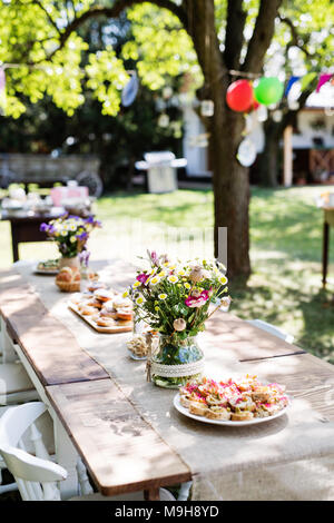 Tabelle für einen Garten Party oder Feier außerhalb. Blumen und Snacks auf dem dekorierten Tisch im Garten. Stockfoto