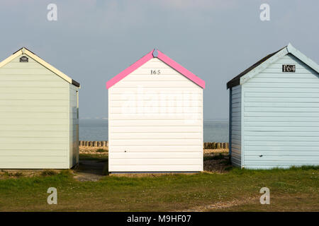 Drei bunten Badekabinen in einer Reihe in Calshot Spit, Southampton, Hampshire, UK mit einem weiblichen Blick auf die Mitte, eine Aussage zu treffen. Stockfoto