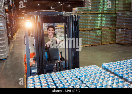 Porträt einer kaukasischen Frauen Lagerarbeiter auf einem Gabelstapler in ein Lager voll von Paletten von aromatisierten Wasser in Dosen. Stockfoto