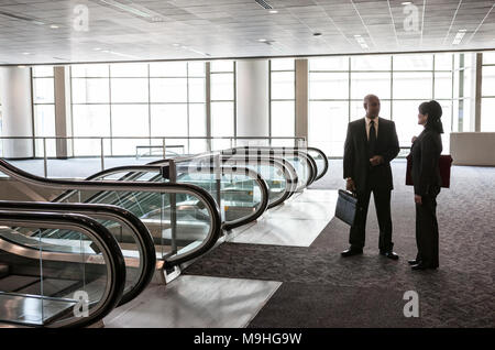 Zwei Geschäftsleute, Mann und Frau, die im Atrium des Gebäudes sprechen. Aktentaschen und Business Anzüge Kollegen sprechen, Kommunikation Stockfoto