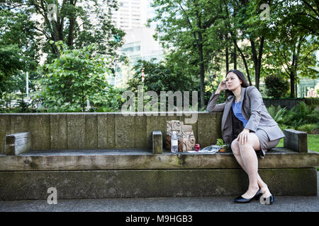 Eine Geschäftsfrau eine Pause in einem Stadtpark, auf einer Bank mit Mittagessen sitzt. Stockfoto