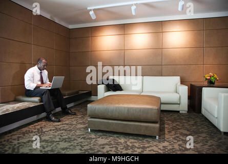 Schwarzer Geschäftsmann auf einem Laptop in der Lobby. Stockfoto