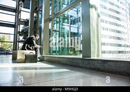 Schwarzer Geschäftsmann auf einem Notebook in einem Wartebereich einer großen, offenen Lobby sitzen. Stockfoto