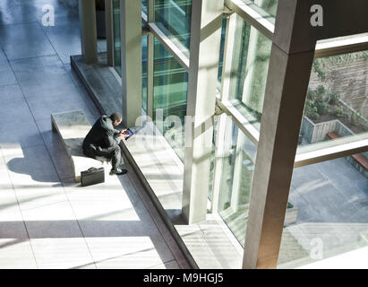 Schwarzer Geschäftsmann auf einem Notebook in einem Wartebereich einer großen, offenen Lobby sitzen. Stockfoto