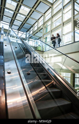 Business Mann und Frau sprechen, an der Spitze einer Rolltreppe in einem großen verglasten Lobby Bereich. Stockfoto