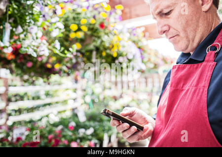 Gartencenter Baumschule Kaukasier Männlich Eigentümer Kontrolle ein Hinweis auf sein Handy in der Baumschule. Stockfoto