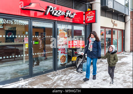 Mutter und Tochter vorbei Pizza Hut in Coventry, West Midlands, UK mit Schnee auf dem Boden. Stockfoto