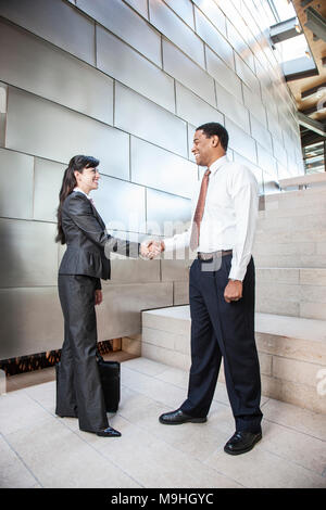 Schwarzer Geschäftsmann und Hispanic Geschäftsfrau in der Lobby eines großen Bürogebäudes. Stockfoto