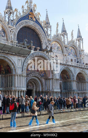 Acqua Alta mit Menschen auf einer passarelle und waten durch Wasser vor der Basilika San Marco, Piazza San Marco, Venedig, Venetien, Italien mit Sun flar Stockfoto