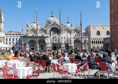 Die Leute im Restaurant sitzen Tische für das Mittagessen in der Piazza San Marco (Markusplatz), Venedig, Italien vor St Marks Basilika (Basilica San Marco) Stockfoto