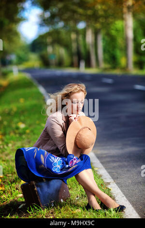 Nachdenkliche Frau sitzt auf einem Koffer Stockfoto