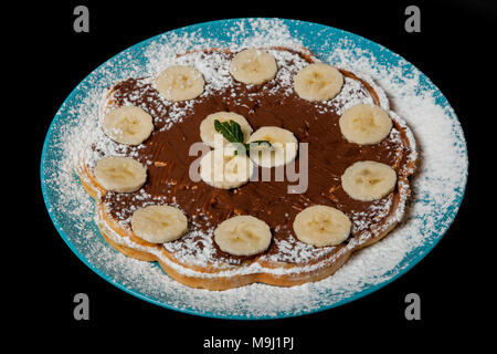 Waffeln mit Schokolade und Banane auf schwarzem Hintergrund. Stockfoto