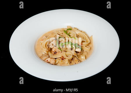 Talifele mit Huhn und Pilzen in einer weißen Platte auf einem schwarzen Hintergrund. Stockfoto