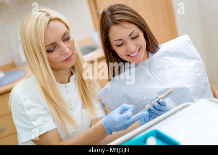 Schöne junge lächelnde Frau zu Besuch in der Zahnarztpraxis und weiblichen Zahnarzt ihre porzellankronen zeigt. Stockfoto
