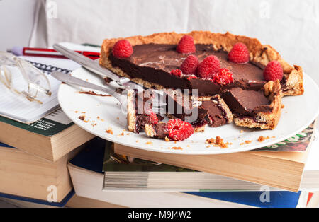 In Scheiben geschnitten und zerbröckelte Schokolade Kuchen und Himbeeren auf einen Stapel Bücher während der Studie Stockfoto