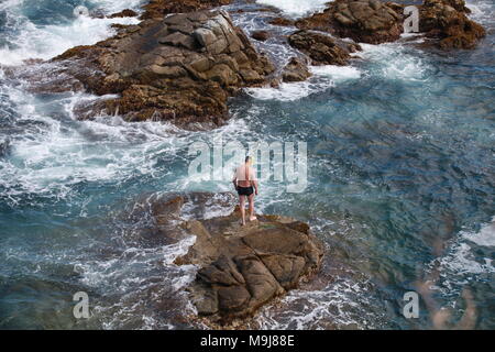 Nicht erkennbare männliche Schwimmer auf einem Felsen vor dem Sprung ins Meer, Ansicht von oben Stockfoto