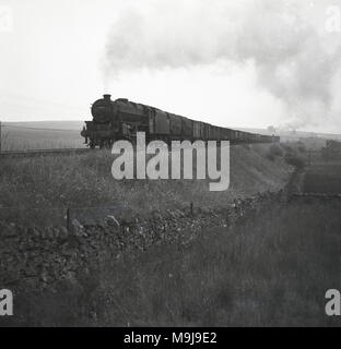 1950, historische Dampflok mit Kutschen fahren auf der Gebankten Landschaft Bahn, England, UK. Stockfoto