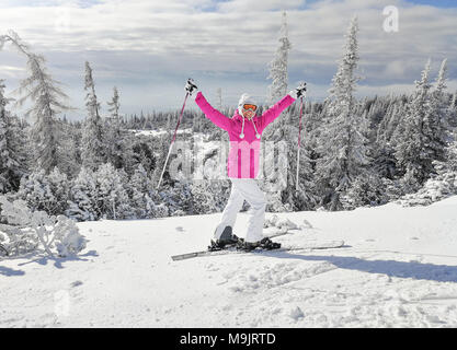 Junge Frau in rosa Winterjacke mit Skiern an den Füßen holding Skistöcke, in der glücklichen Pose lächelnd bei schönem sonnigen Wintertag. Skigebiet Strbske pleso Resor Stockfoto