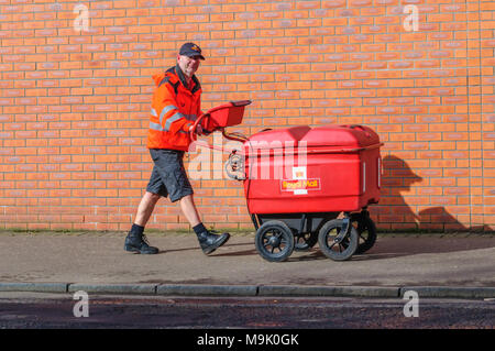 Royal Mail Briefträger, gekleidet in seine Uniform in Shorts und schob einen Trolley und die Bereitstellung der e-mail in Glasgow, Schottland, Großbritannien Stockfoto