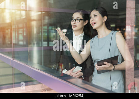 Asian Business Supervisor erklärt das neue Projekt der Mitarbeiter neben dem Fenster. Sie sind sowohl interessant mit dem Programm und tragen für Stockfoto