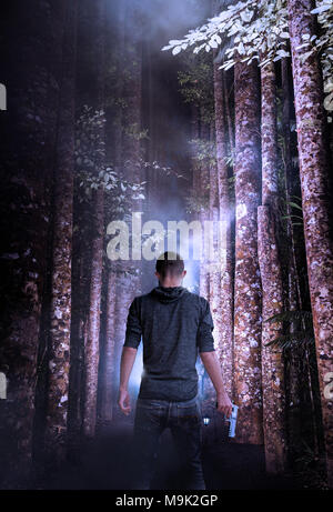 Lone Gunman Holding eine silberne Pistole auf seiner Seite Schuß von hinten in eine erie Wald Stockfoto