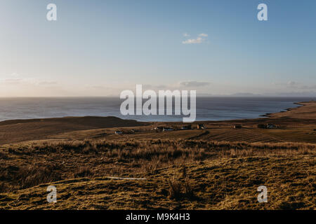 Blick auf die Landschaft und ein kleines Dorf an der Küste auf der Insel Skye, Schottland, während der Goldenen Stunde. Stockfoto